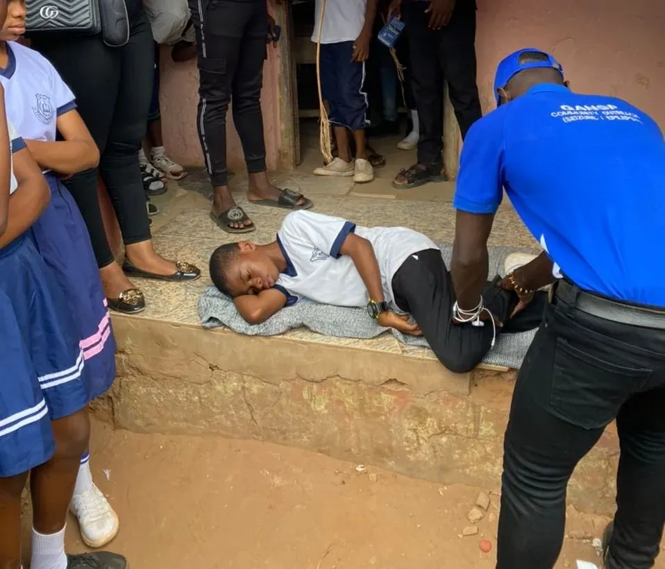 A volunteer shows students seizure first aid, with a student lying on his side on the floor