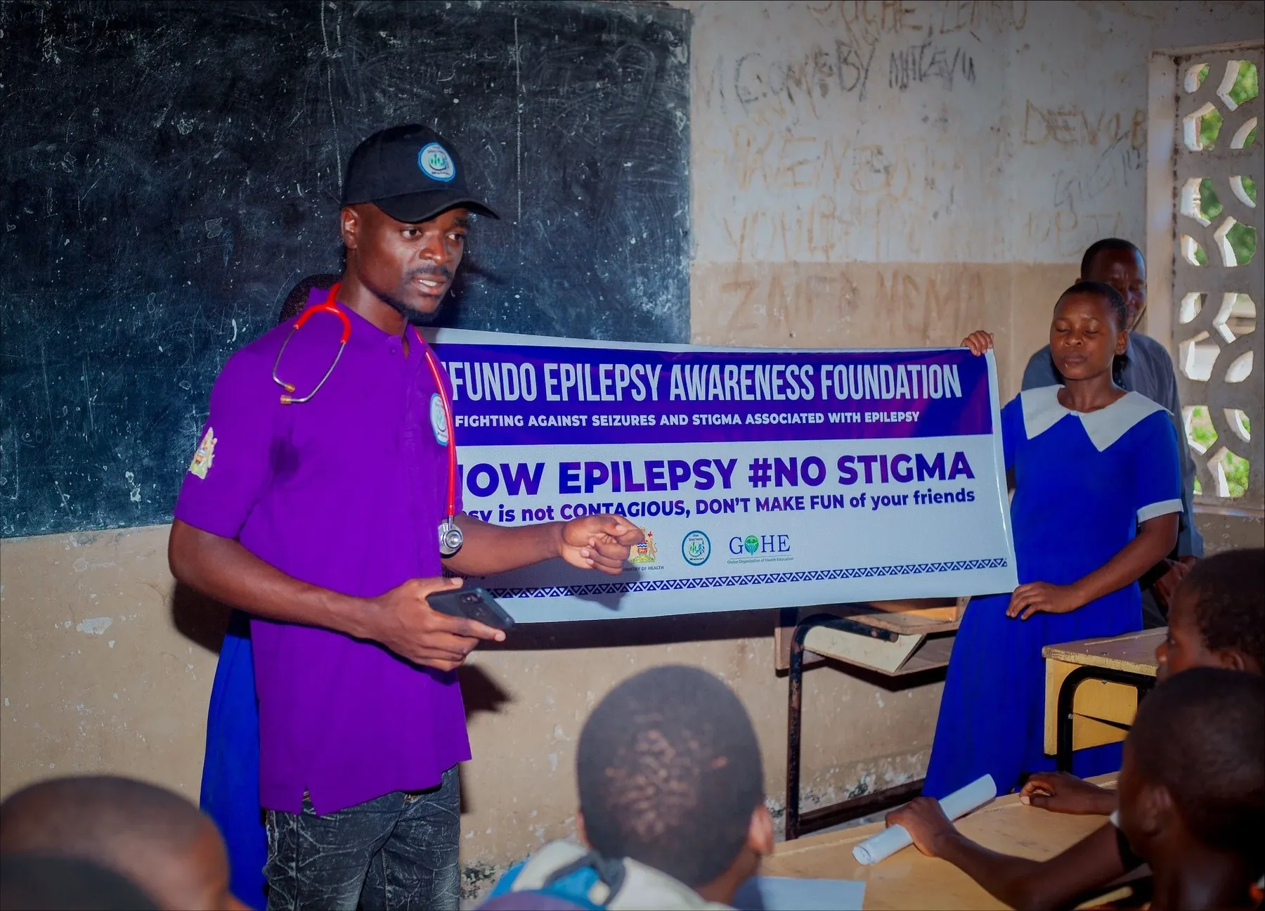 An epilepsy lesson in a Malawi classroom. A banner behind the teacher reads #NO STIGMA, epilepsy is not contagious.